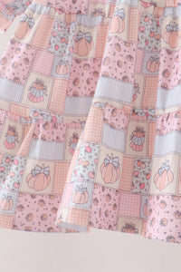 A close-up of a tiered skirt featuring a patchwork print of pink pumpkins, gingham checks, and floral motifs in pastel shades of pink, beige, and light blue.
