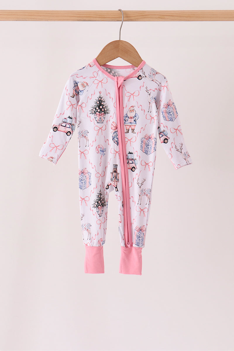 A baby long-sleeve footless zip-up sleeper hanging on a wooden hanger against a light beige background. The sleeper is white with a pink zipper, pink trim, and a festive holiday print featuring pink bows, Santa Claus, snowman, Christmas trees, and small vehicles.