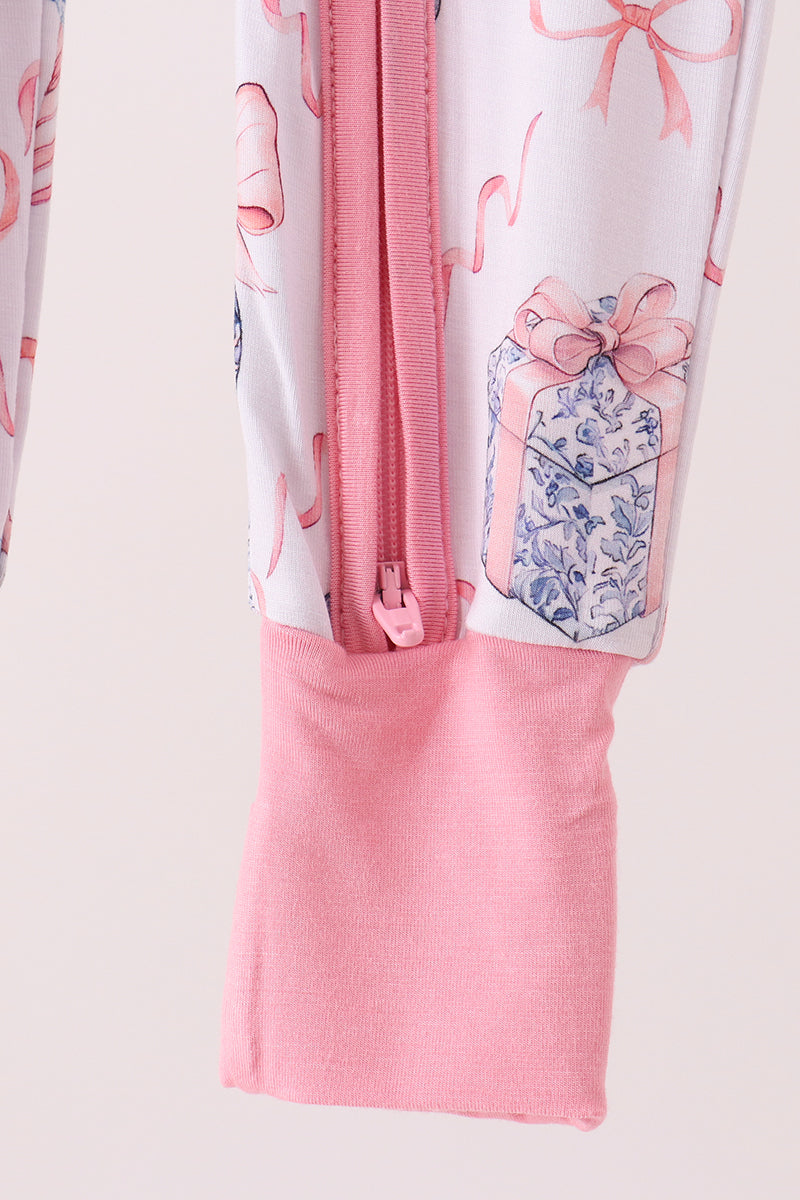 Close-up of a children's zip-up garment with a pink zipper, pink ribbed cuffs, and a white body printed with pink ribbon motifs and a blue-and-white gift box design.