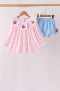 Pink gingham top with turkey embroidery on white collar paired with blue bloomer shorts hanging on a rack.