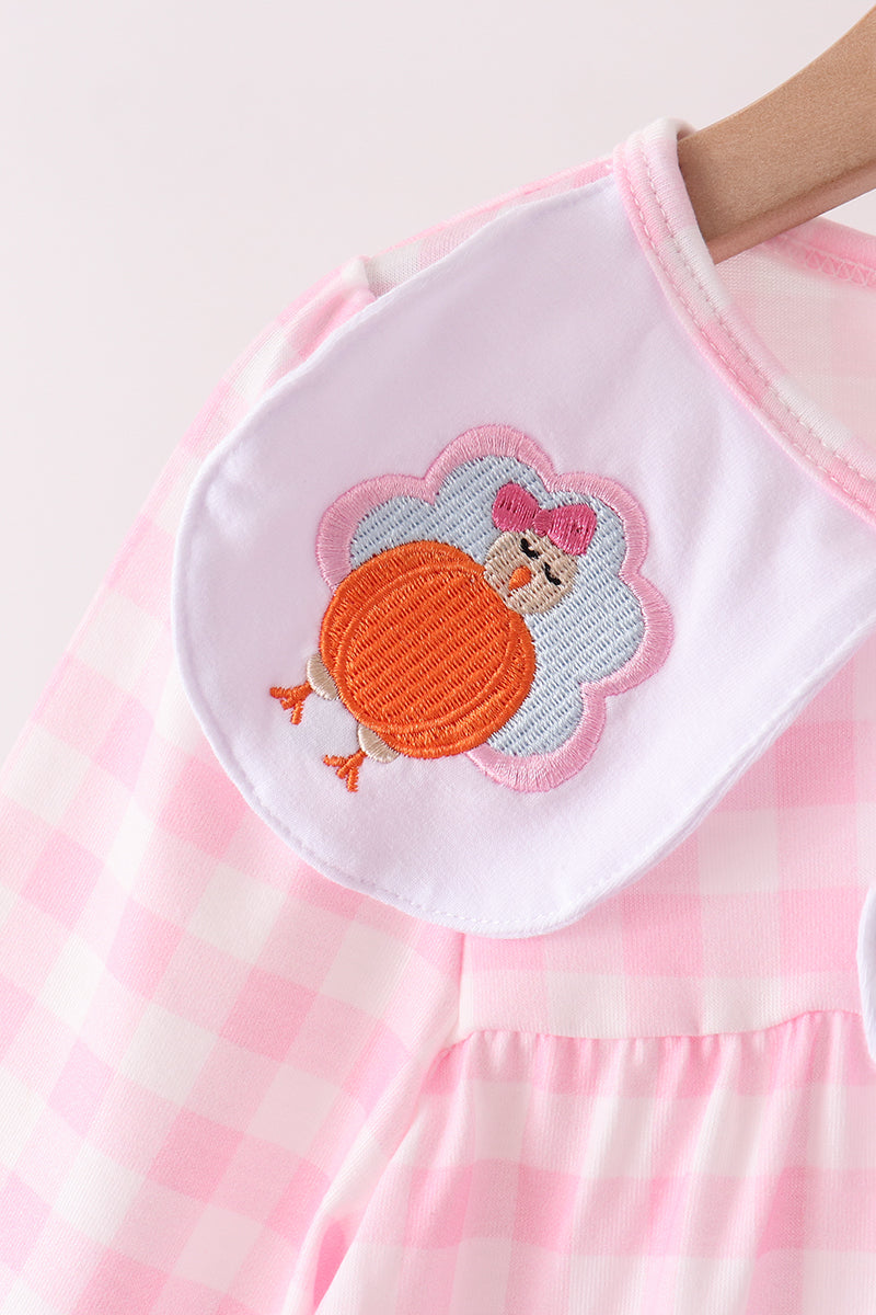 Pink gingham children's garment featuring a cute embroidered turkey with a bow on a white patch.