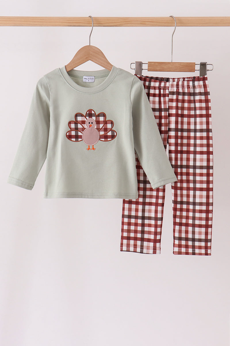 Sage green long-sleeve top with turkey applique and rust plaid pants hanging on wooden hangers