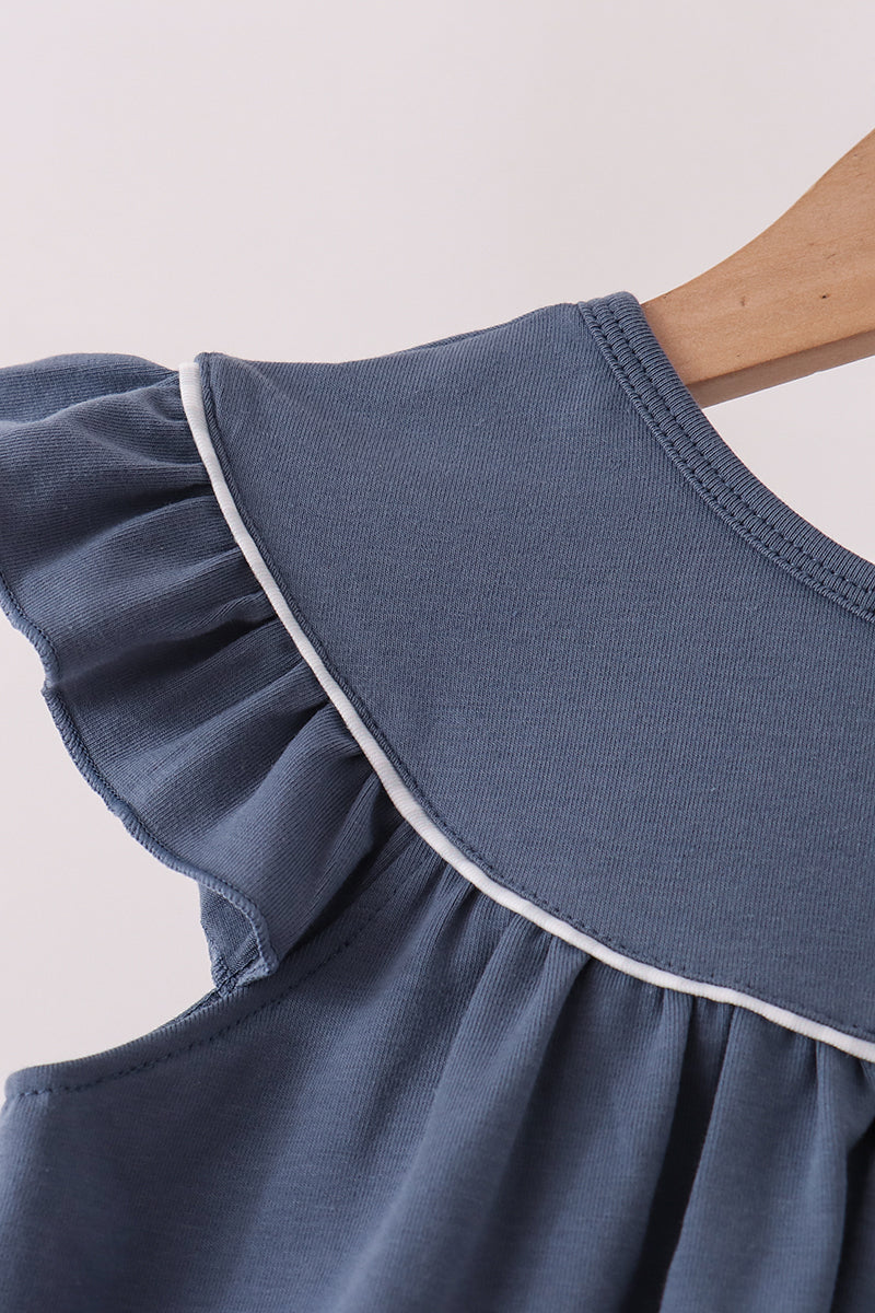 Close-up of a blue ruffled sleeveless top or dress on a wooden hanger, showing a wide collar with white piping trim against a light background.