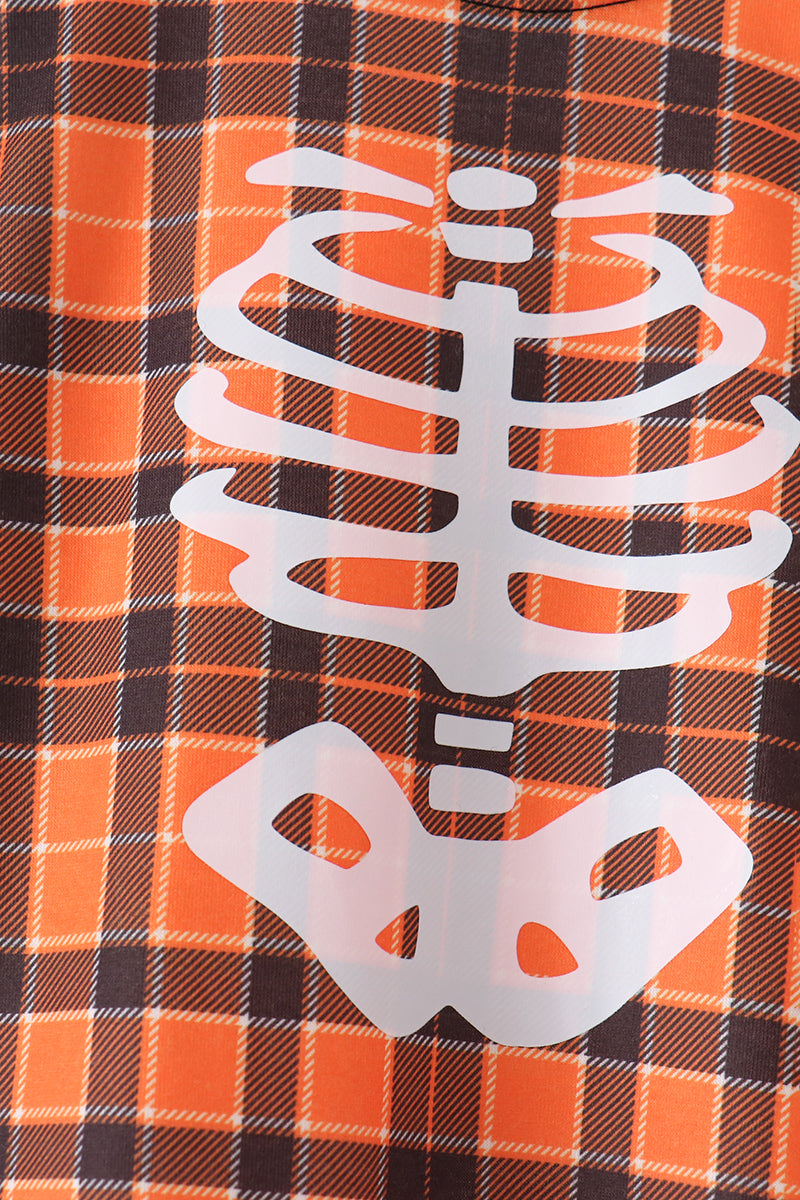 Close-up of a Halloween-themed shirt featuring an orange and black plaid pattern with a large white skeleton rib cage and pelvis graphic.