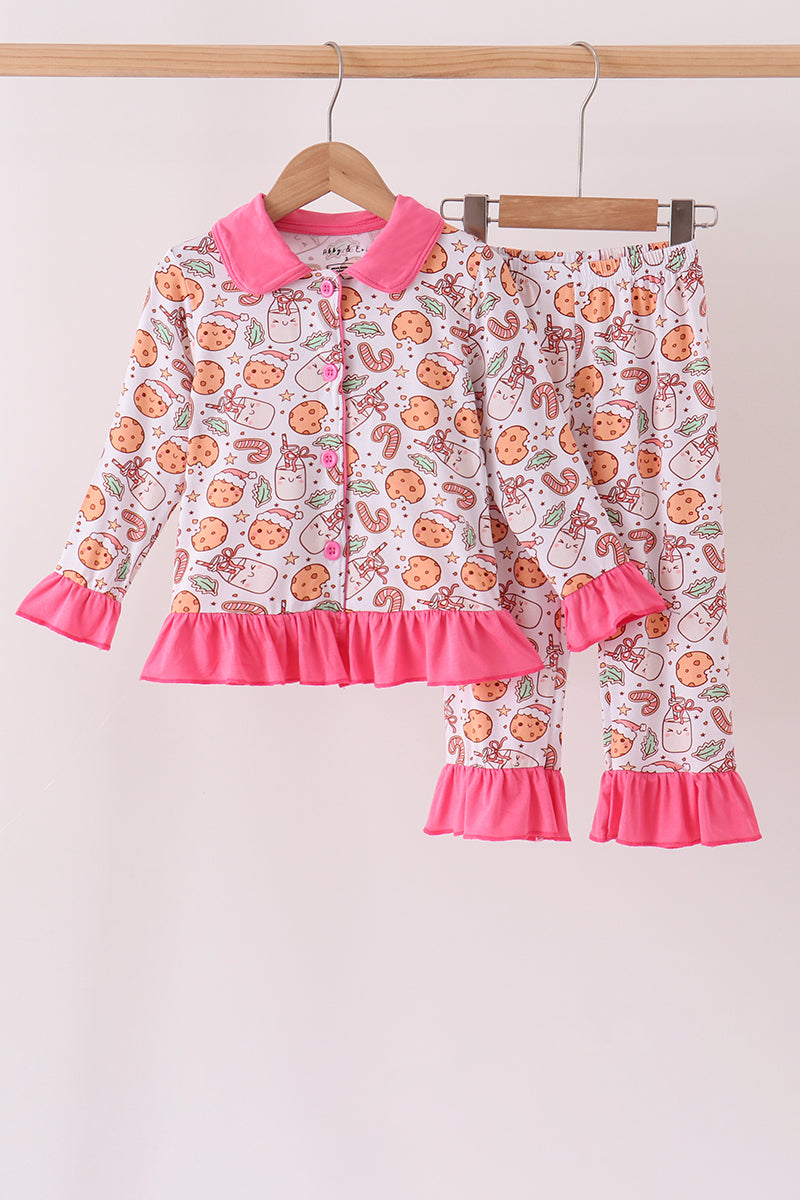 A two-piece children's pajama set hanging on wooden hangers against a plain light background. The set includes a long-sleeve button-front top and matching pants, both in a white base with an all-over orange cookie print, bright pink collar, cuffs, and hem, and a pink button closure.