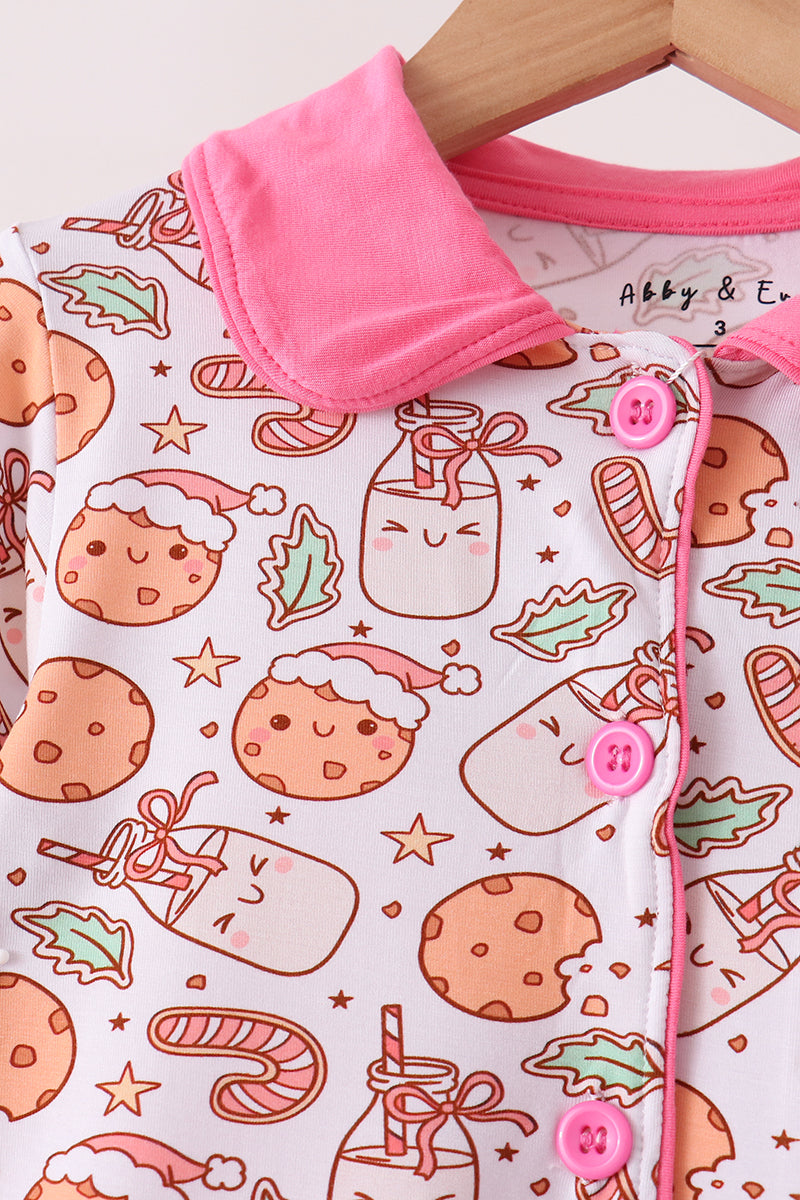 A close-up of a baby garment featuring a cute holiday print with cookies, candy canes, and mason jars on a white background, accented with a bright pink collar and pink buttons. The brand name 'Abby & E' is visible on the inner neck label.