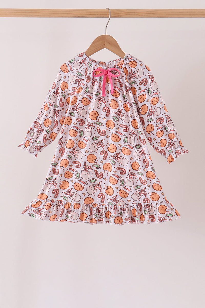 A long-sleeve baby dress with a white base and an all-over orange and green pattern, featuring a pink bow at the neckline, hanging on a wooden hanger against a light beige wall.