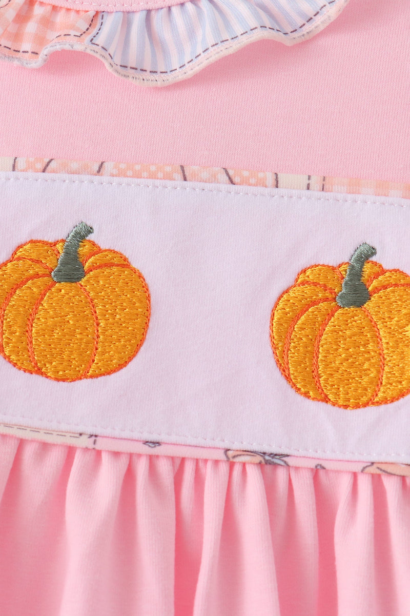 Close-up of a pink dress with a white band featuring two embroidered orange pumpkins with green stems.
