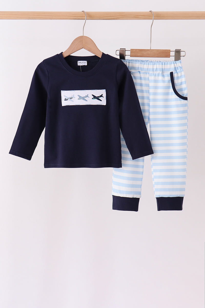 Navy long-sleeve top with airplane patch and striped pants hanging on wooden hangers