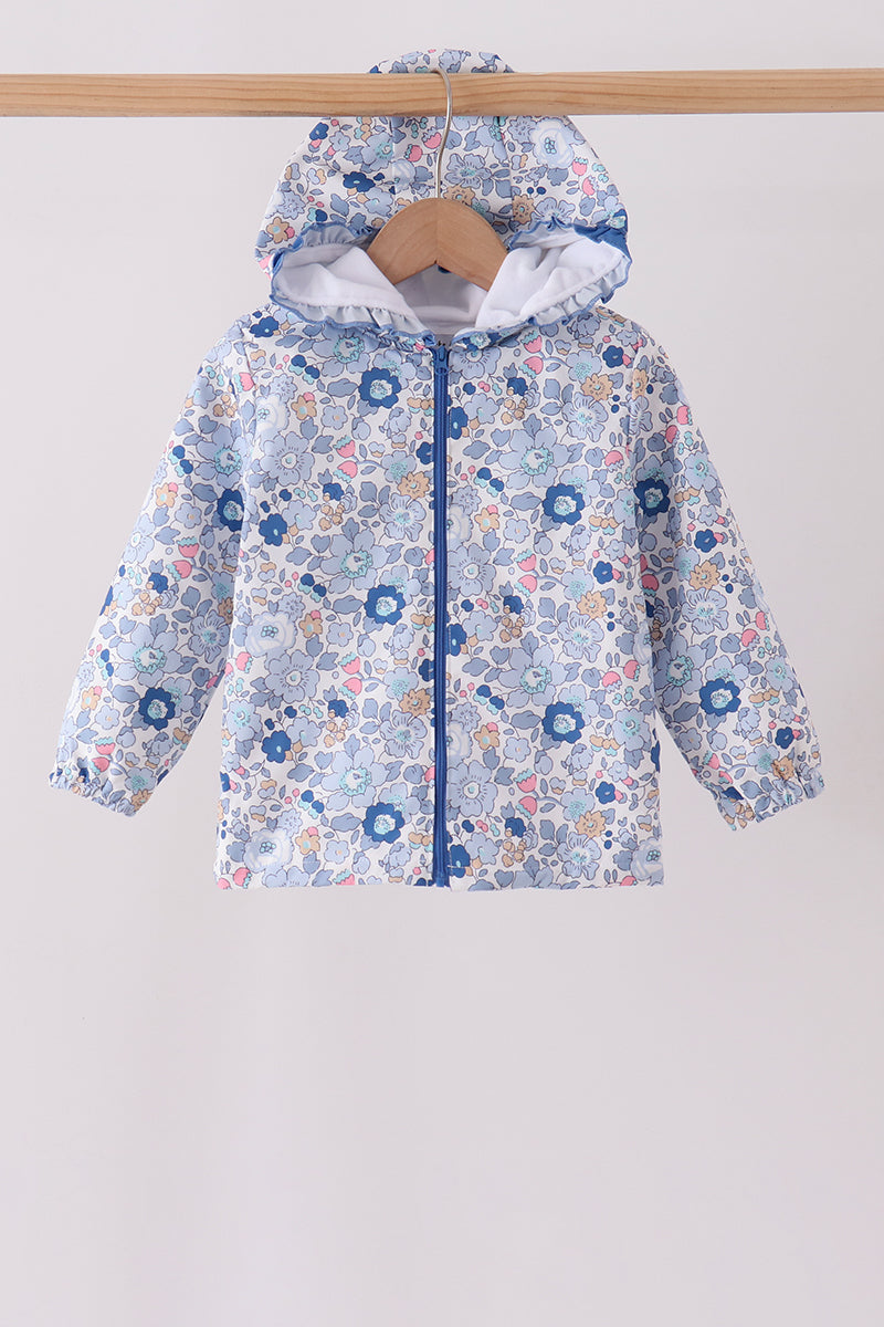 White baby raincoat with blue floral print and pink accents hanging on a wooden hanger against white