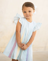 Little girl wearing a light blue swing dress with flutter sleeves and colorful rainbow pleated stripes down the front.