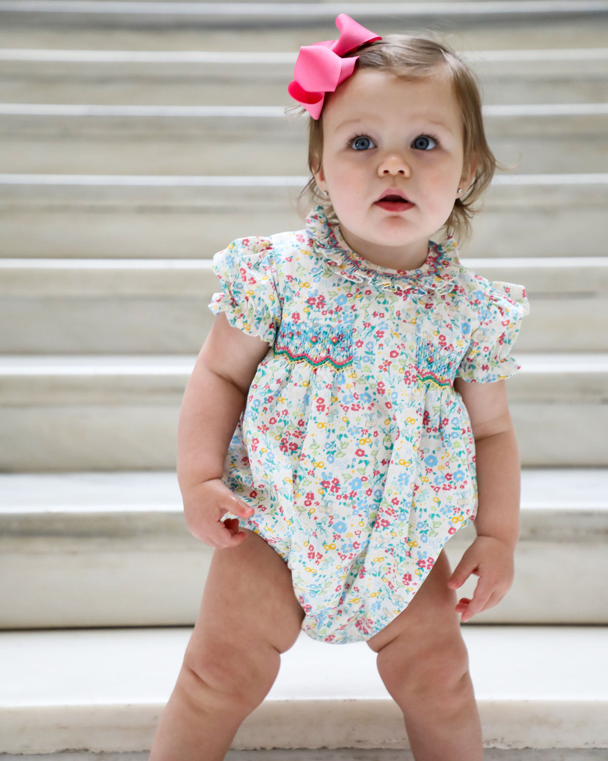 Front view of baby in floral romper displaying round smocked bodice and petal collar