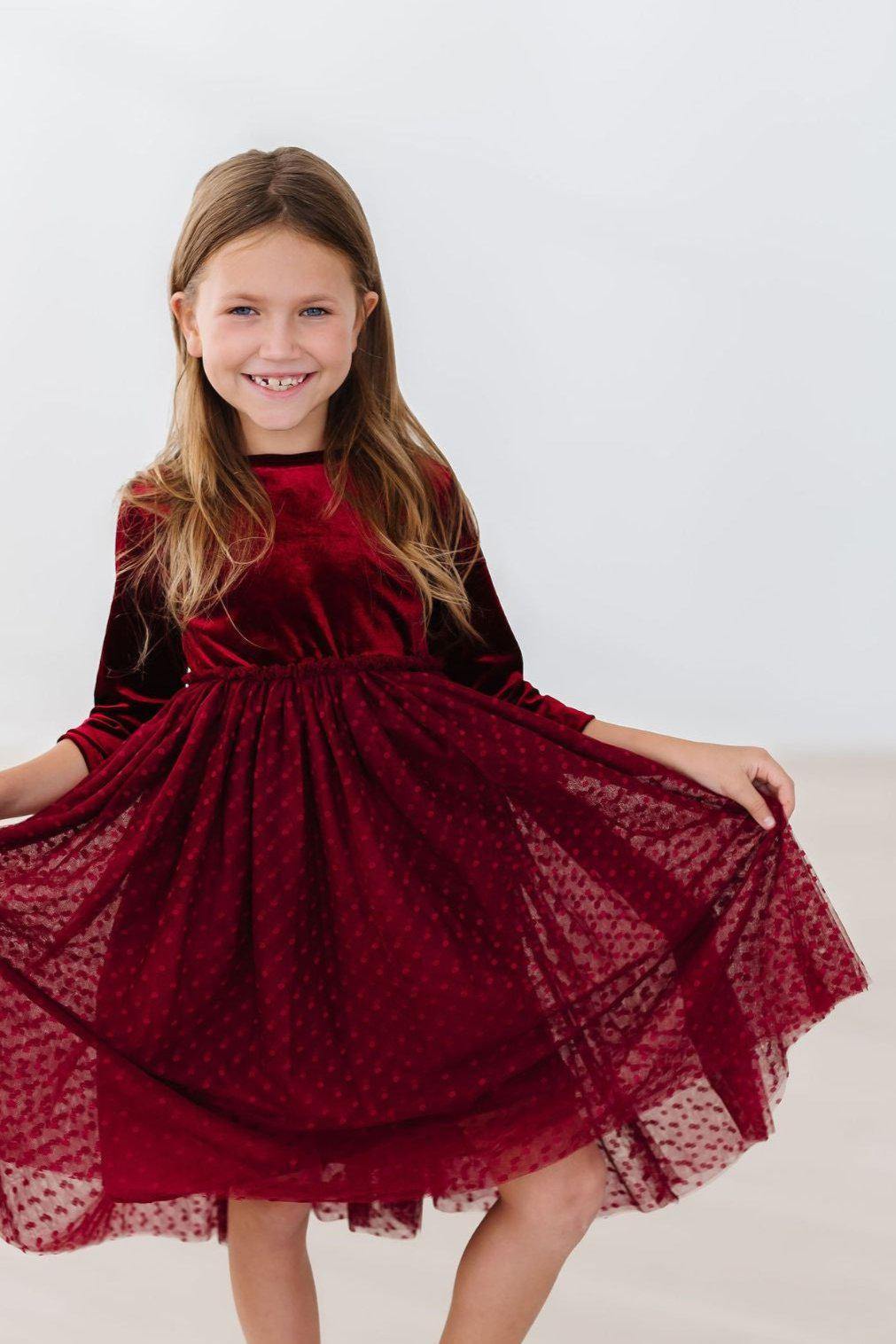 A young girl wearing a Cranberry Velvet Tutu Dress, smiling and twirling, showcasing the elegant design and full tulle skirt.