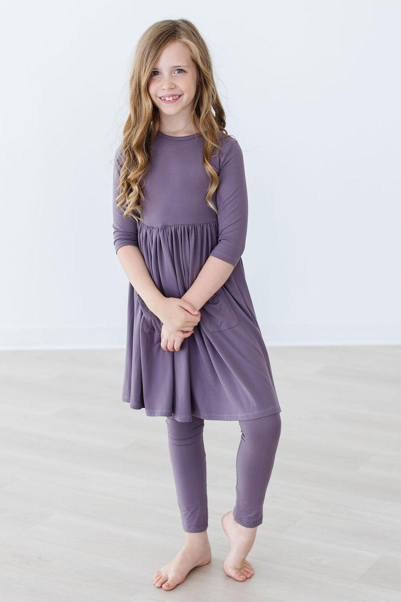 Young girl posing confidently in a Vintage Violet 3/4 Sleeve Pocket Twirl Dress by Mila & Rose, with playful curls and a cheerful expression.