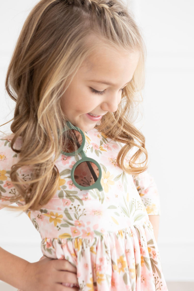Charming young girl in a Pretty Peachy 3/4 Sleeve Pocket Twirl Dress from Mila & Rose, showcasing her adorable style while wearing playful sunglasses.
