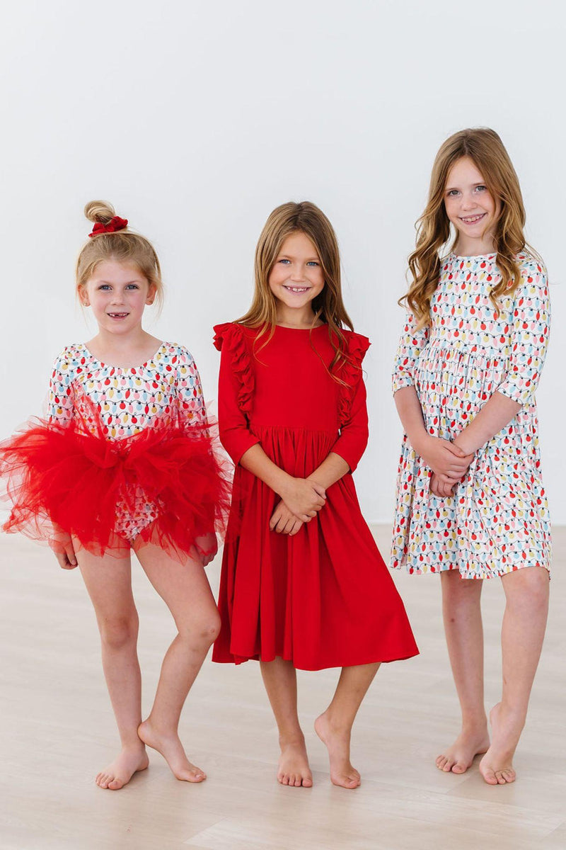 Three girls showcasing the Merry & Bright 3/4 Sleeve Pocket Twirl Dress by Mila & Rose®, including a vibrant red dress, perfect for holiday festivities and fun.