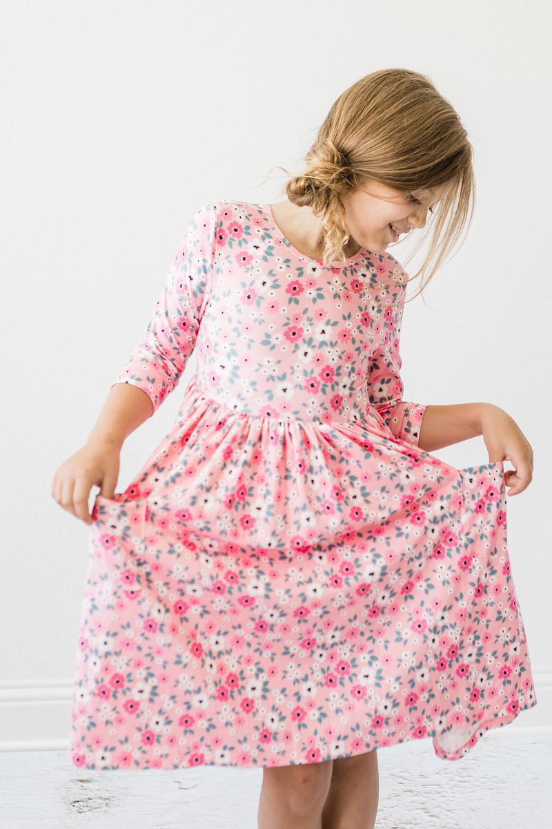 Girl joyfully lifting her Azalea 3/4 Sleeve Pocket Twirl Dress, displaying its full skirt and vibrant floral print.