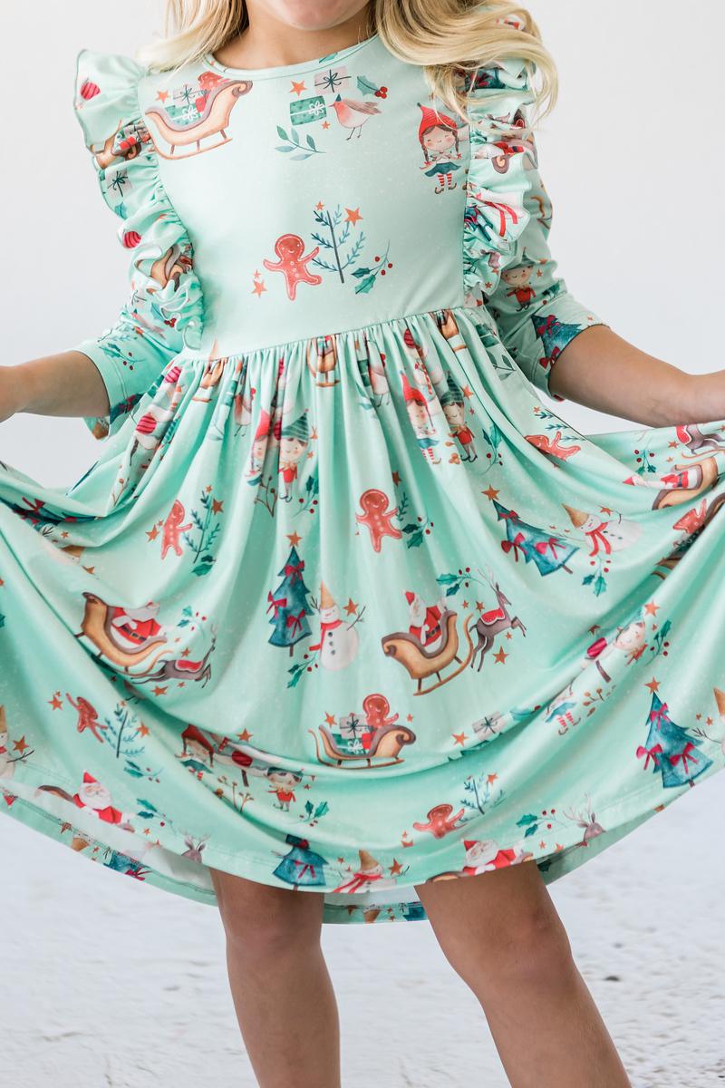 Believe in Your Elf 3/4 Sleeve Ruffle Twirl Dress displayed on a child, featuring playful patterns of gingerbread men and holiday decorations.