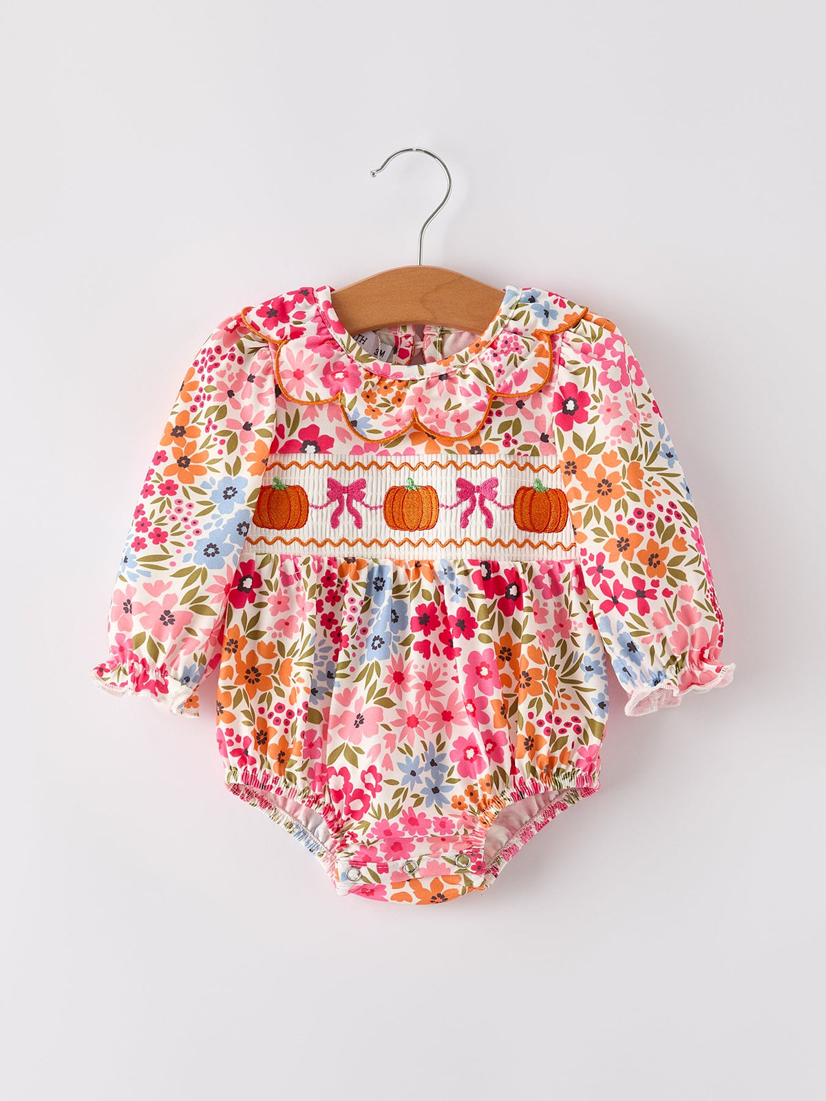Fall floral baby romper with pumpkin embroidery, bow smock, and scalloped trim on a hanger.