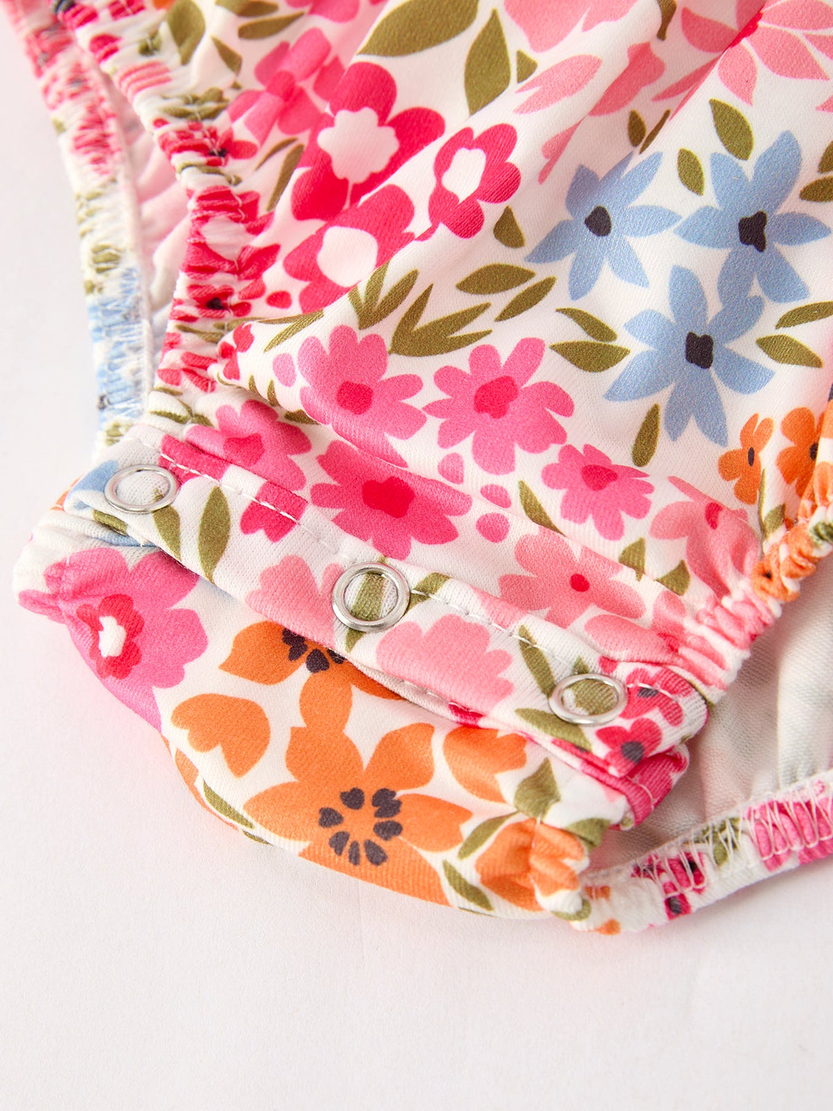 Floral print baby girl romper with pink, orange, and blue flowers, smocked waist and metal snap rings.
