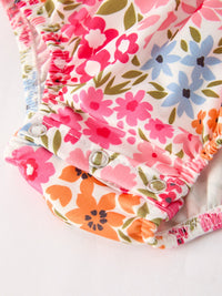 Floral print baby girl romper with pink, orange, and blue flowers, smocked waist and metal snap rings.