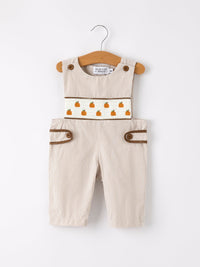 Beige checkered boys romper with pumpkin embroidery on a white smocked panel and brown trim.