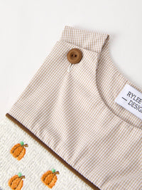Beige striped smocked romper with pumpkin embroidery and brown button detail.