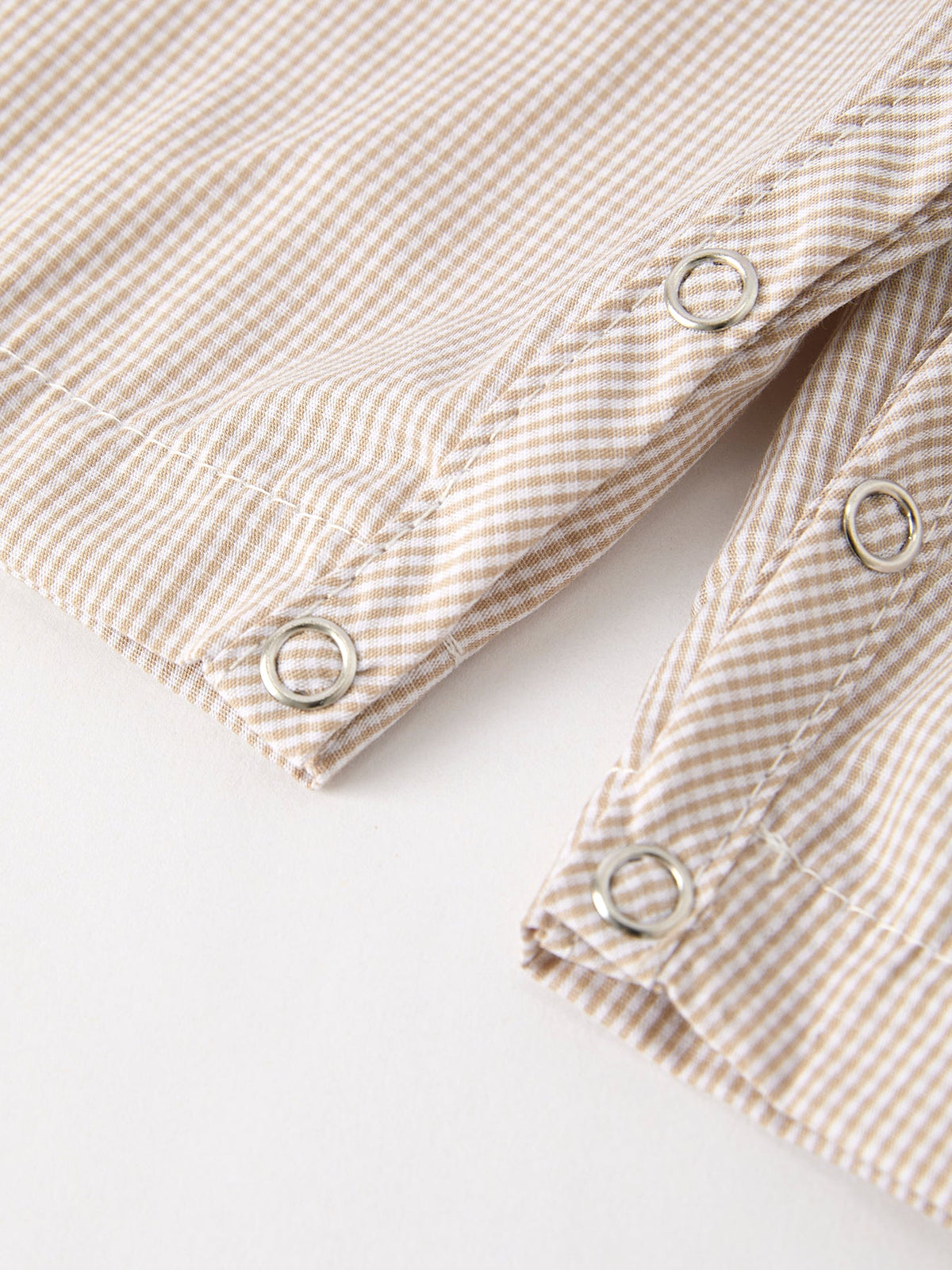Close-up of beige striped romper fabric with silver snap buttons, part of fall pumpkin smock boys romper.