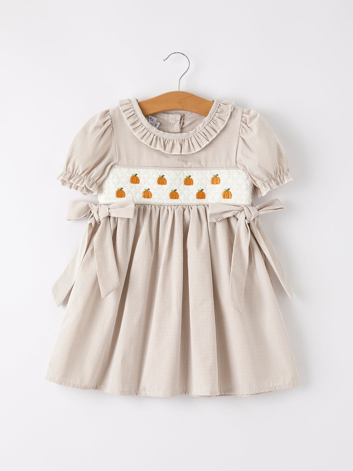 Beige plaid girls' dress with pumpkin embroidery on a smocked panel, puff sleeves, and waist ties