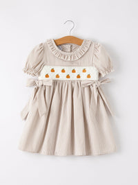 Beige plaid girls' dress with pumpkin embroidery on a smocked panel, puff sleeves, and waist ties
