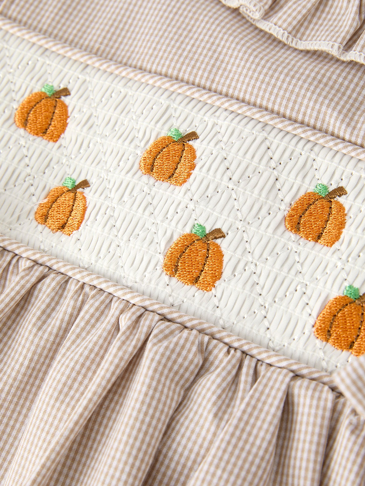 Beige striped smock border with white quilt panel featuring orange pumpkin embroidery for a fall girls' dress.
