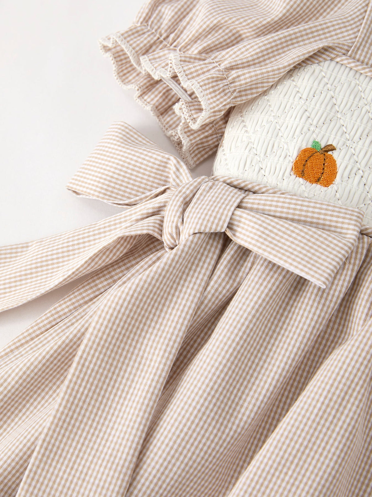 Beige plaid smock dress for girls with pumpkin embroidery and tied waist bow.
