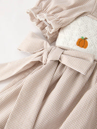 Beige plaid smock dress for girls with pumpkin embroidery and tied waist bow.