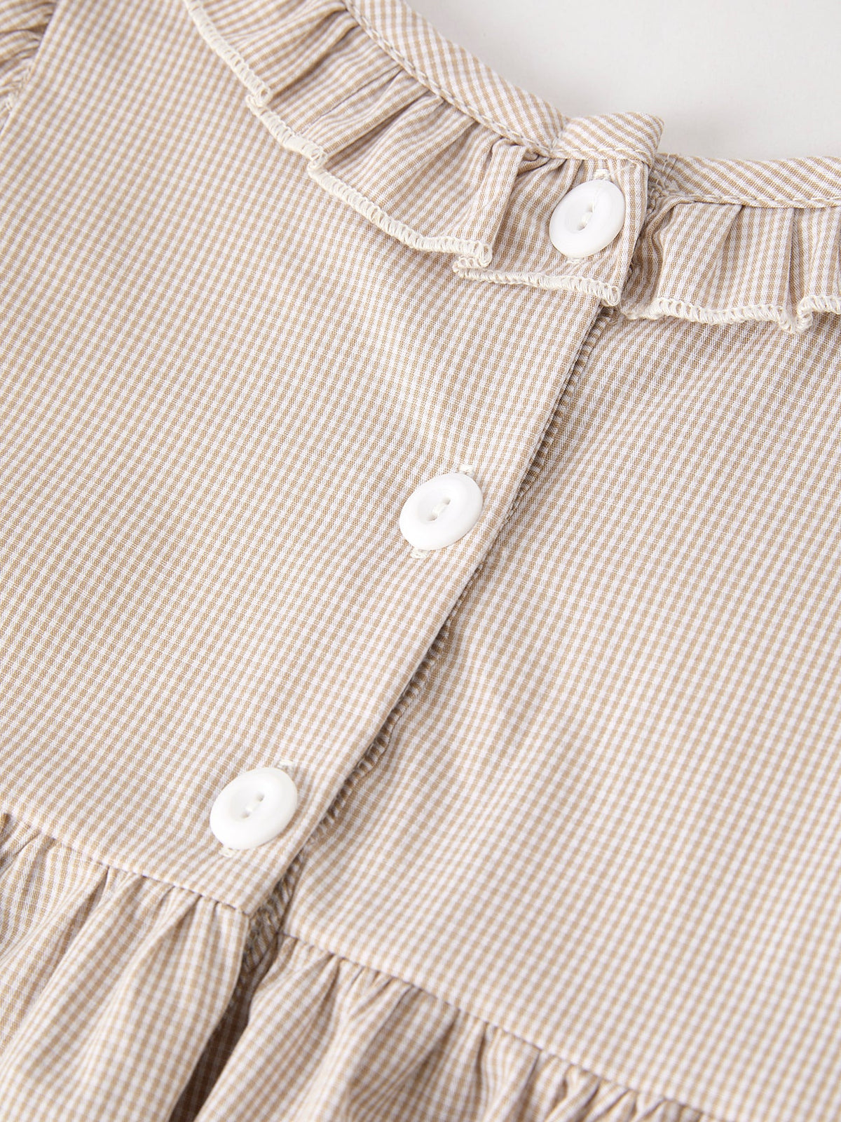 Beige plaid smock dress close-up with white buttons and gathered waist detail.
