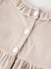 Beige plaid smock dress close-up with white buttons and gathered waist detail.