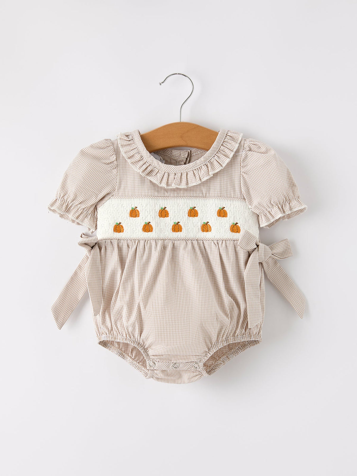 Beige plaid baby girl romper with pumpkin embroidery on smocked panel and waist bow.