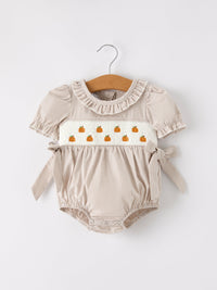 Beige plaid baby girl romper with pumpkin embroidery on smocked panel and waist bow.