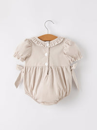 Beige plaid baby girl romper with puff sleeves, ruffled collar, front buttons, and tied sides.