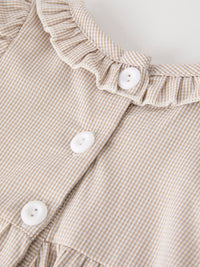 Beige plaid baby romper with ruffle trim and white buttons up the front.