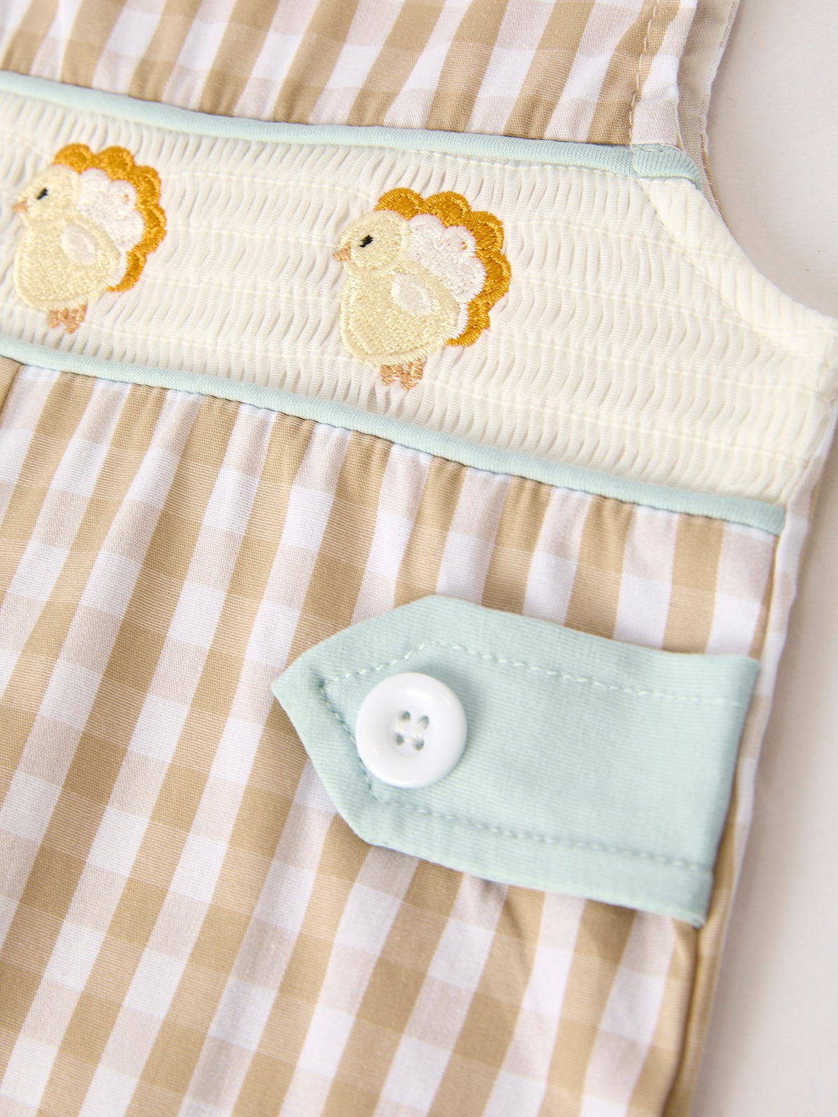 Apricot plaid baby romper featuring smocked chest with festive chick embroidery and mint green button tab detail.