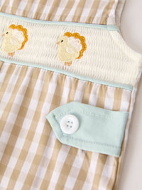 Apricot plaid baby romper featuring smocked chest with festive chick embroidery and mint green button tab detail.