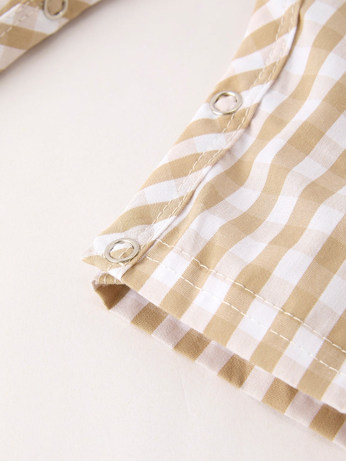 Apricot and white plaid baby romper fabric detail with silver snap buttons and neat stitching.