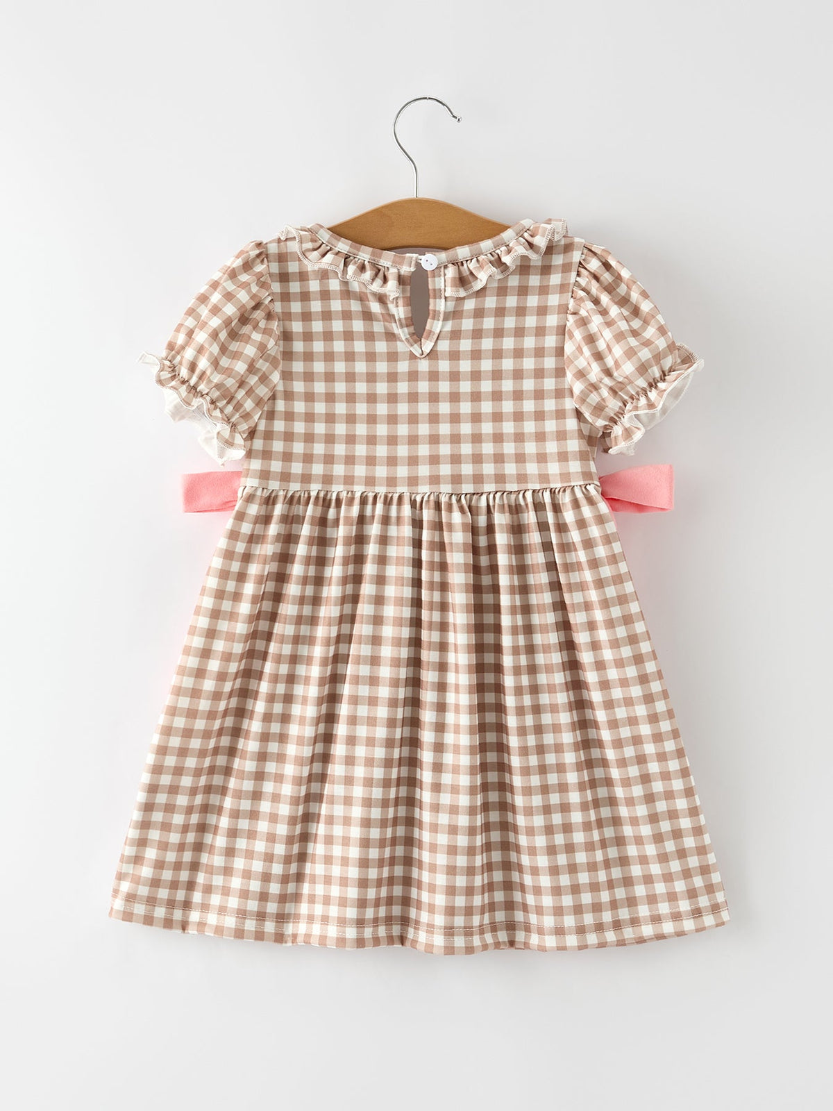 Beige gingham plaid dress with puff sleeves, ruffled neckline, and pink waist bows on a hanger.