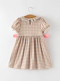 Beige gingham plaid dress with puff sleeves, ruffled neckline, and pink waist bows on a hanger.