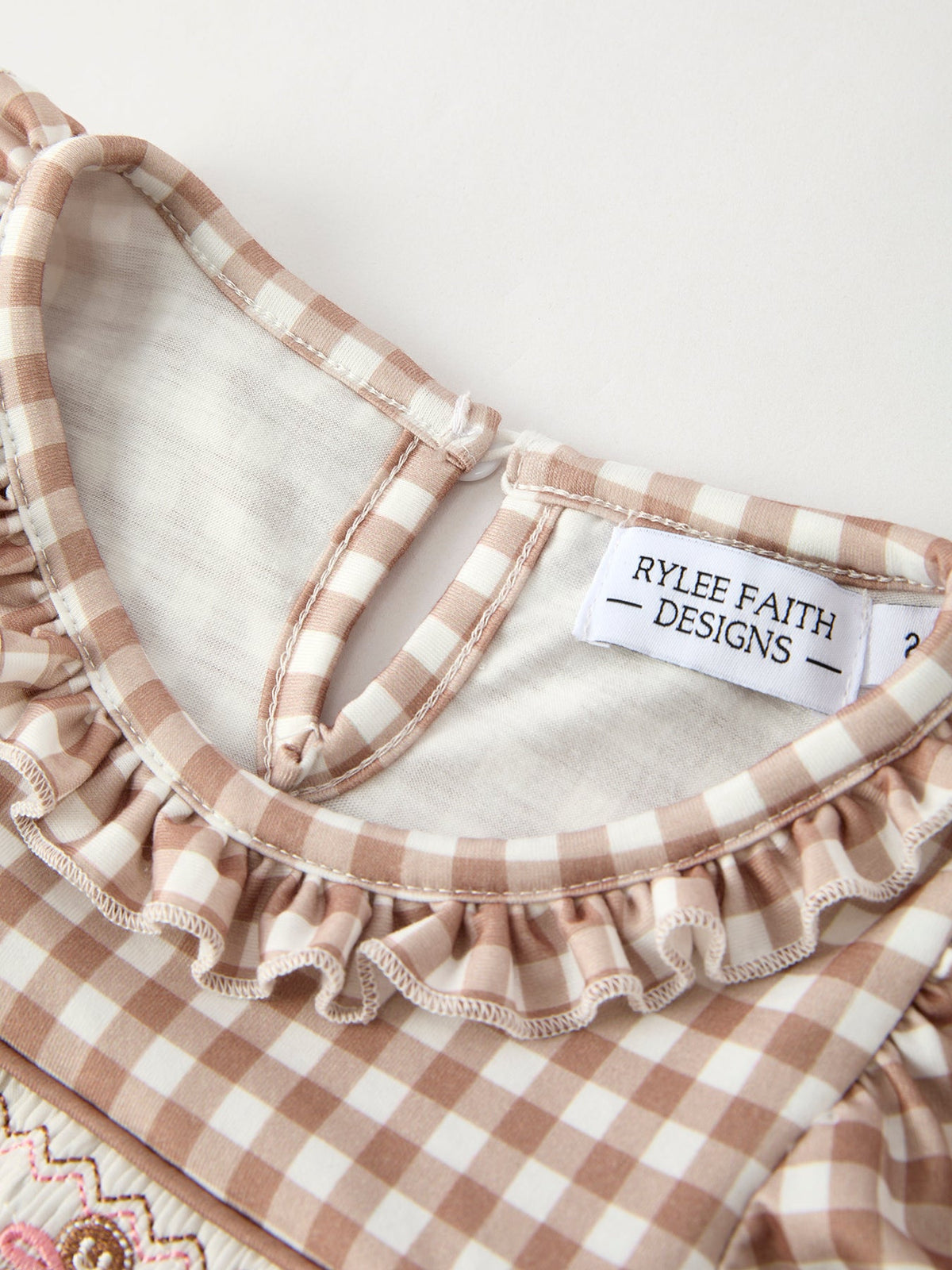 Close-up of Christmas vintage-style plaid dress with ruffled edge and Rylee Faith Designs label.