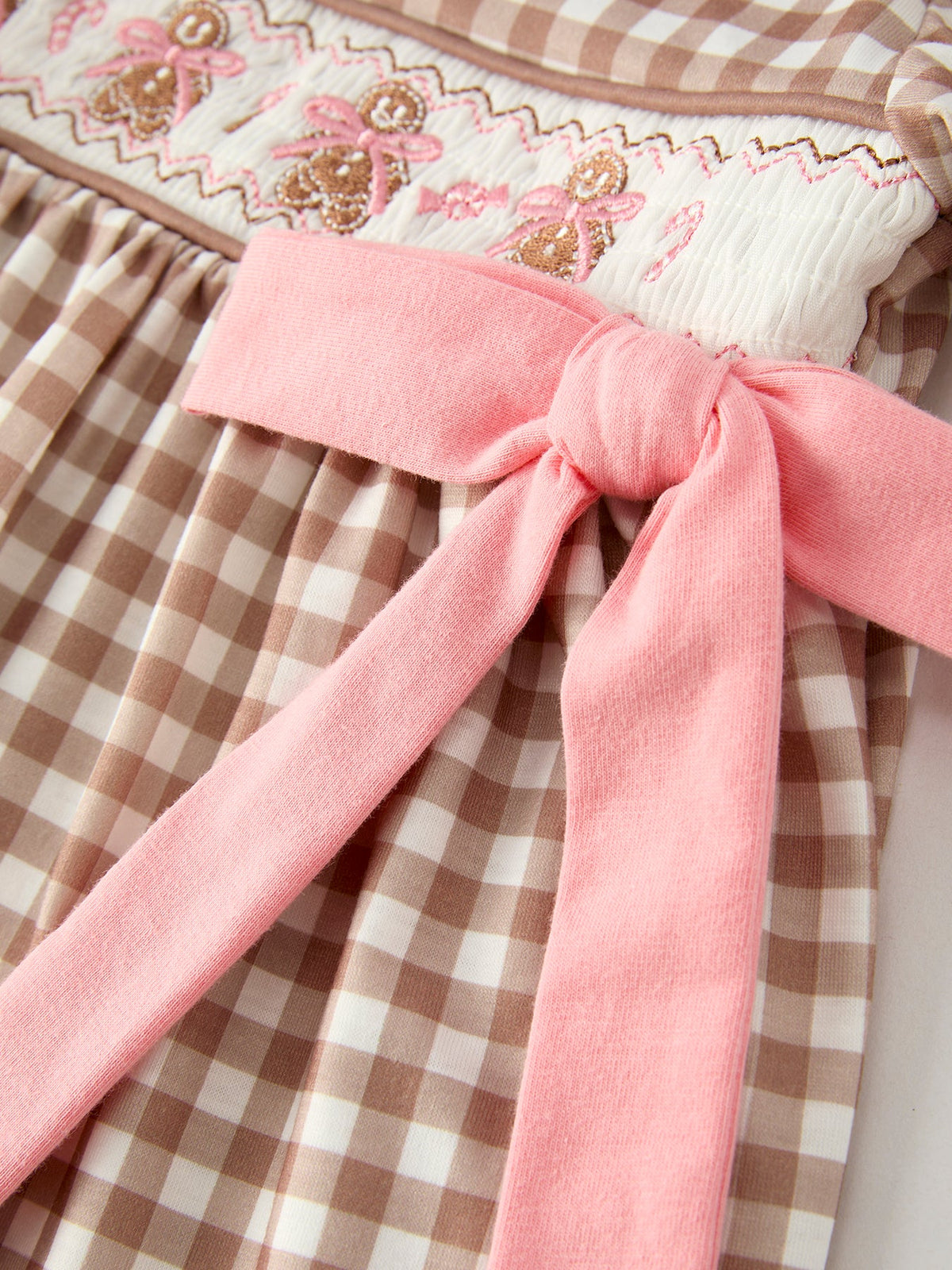 Close-up of Christmas vintage-style plaid dress with pink sash, smocked bodice, and embroidered gingerbread bows