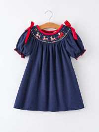 Navy Christmas dress with Santa sleigh embroidery, reindeer motif, and red ribbon shoulder ties. Festive holiday party outfit.
