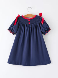 Navy Christmas girl dress with red bows on shoulders, red button back, and smocked neckline for holiday celebrations.