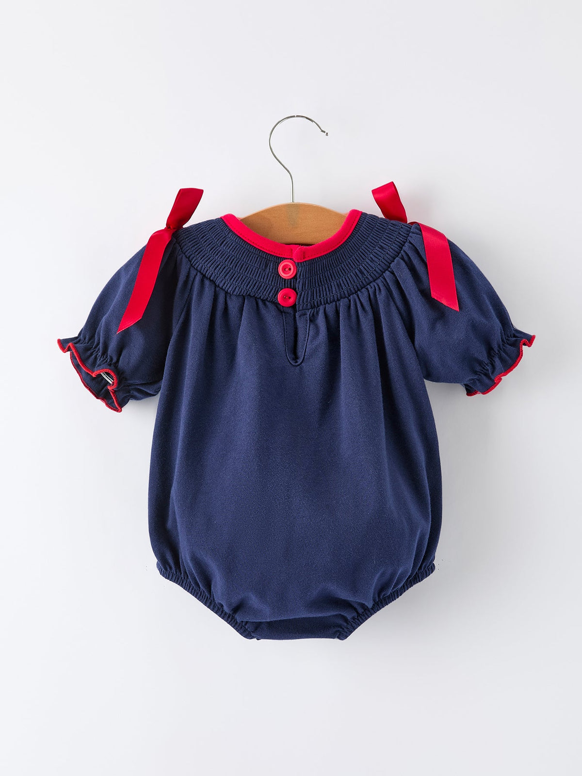 Navy baby girls romper with red ribbon shoulder ties, red collar trim, and front buttons for festive holiday wear.
