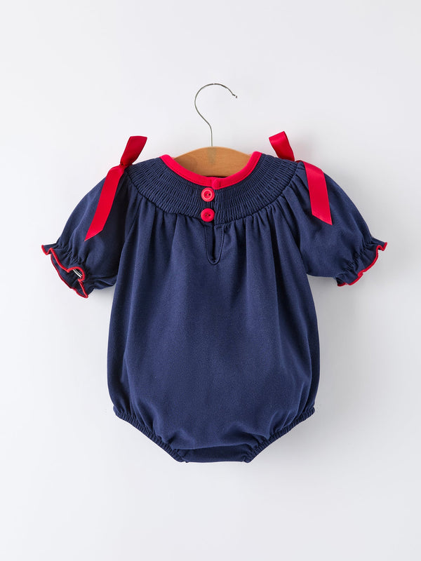 Navy baby girls romper with red ribbon shoulder ties, red collar trim, and front buttons for festive holiday wear.
